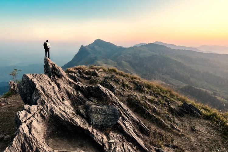 Traveller hike on the peak of rocks mountain at sunset, success,winner, leader concept